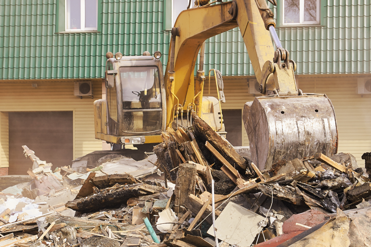 Industrial backhoe on a job site, performing complete demolition services on a house.