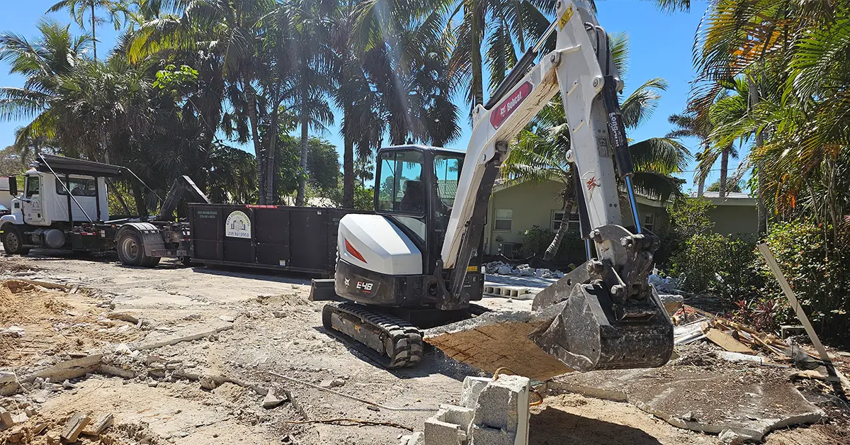 Parking-space dumpster available for same-day delivery from Eco Demolitions, featured here alongside a Bobcat backhoe ripping up a concrete foundation.
