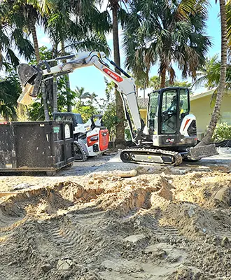 Eco Demolitions backhoe working on a job site, ripping out the concrete foundation of a building in Southwest Florida and disposing of the materials in a nearby dumpster.