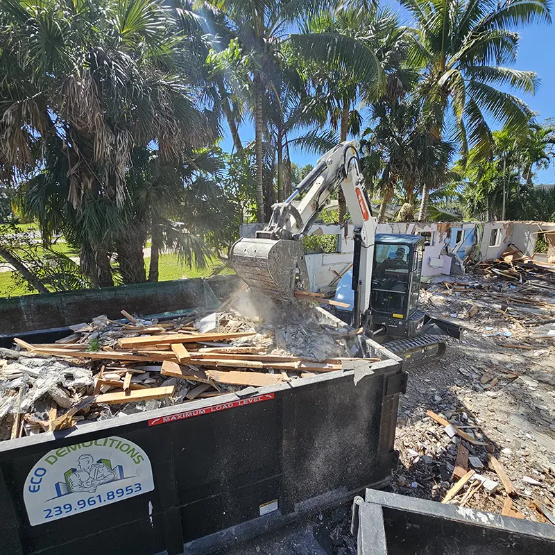 An Eco Demolitions Bobcat backhoe working on a residential job site in Southwest Florida, dumping a bucket-load of construction materials into an efficient dumpster.