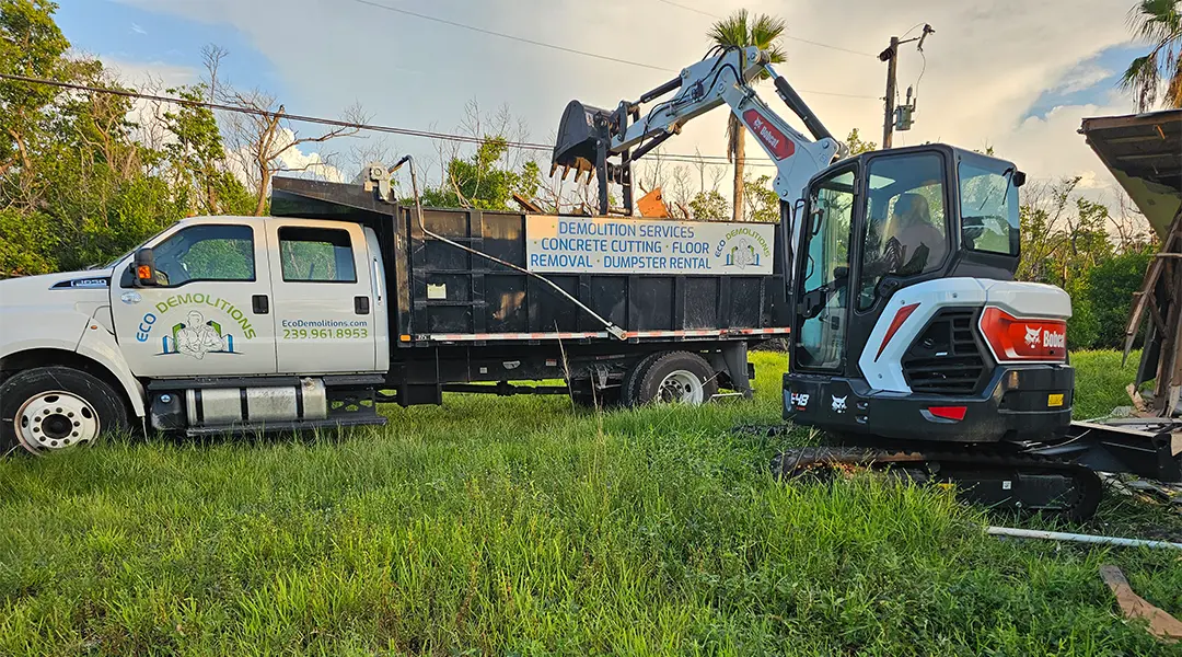 An Eco Demolitions Bobcat backhoe working on a residential job site in Southwest Florida, dumping building debris into a nearby dumpster truck.