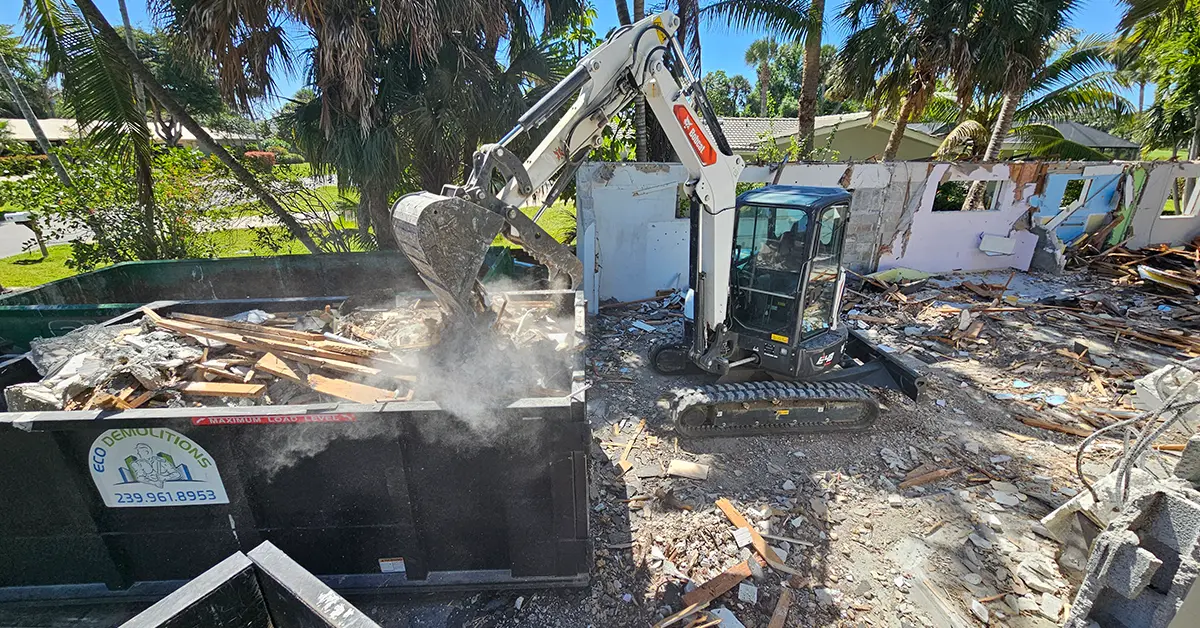 A Bobcat backhoe filling a compact dumpster at an Eco Demolitions job site with construction debris.