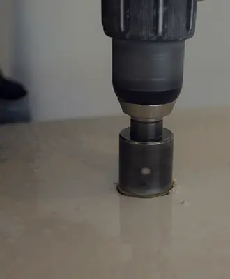 Cutting a utility core in a concrete counter top with a water-cooled diamond-bit drill bit to prevent dust particles from flying.
