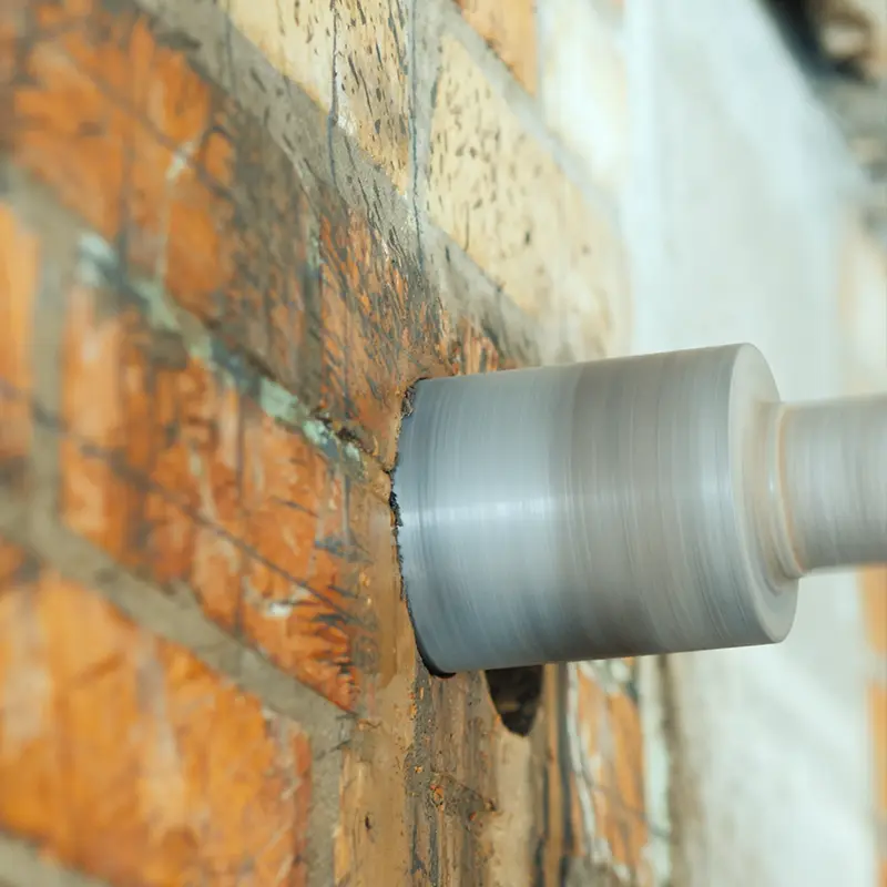 Close-up photo of a diamond-tipped drill bit coring a hole through a brick wall.
