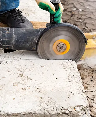 Close-up of a worker using a specialized circular saw to cut through concrete on a job site.