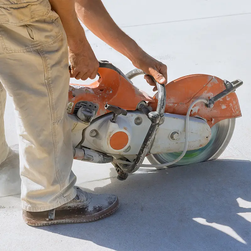 Construction worker using a specialized saw to cut through a concrete foundation.