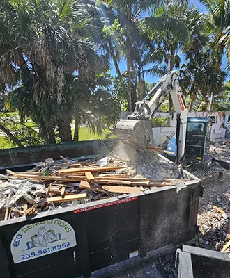 Eco Demolitions backhoe working on a job site, tearing down a house in Southwest Florida and neatly disposing of the materials in a dumpster.