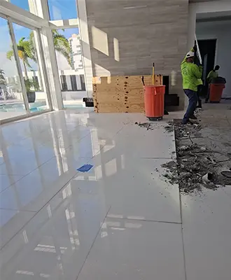 Tile flooring removal being performed at an affluent house in Southwest Florida with a pool deck and palm trees visible through the floor-to-ceiling windows.