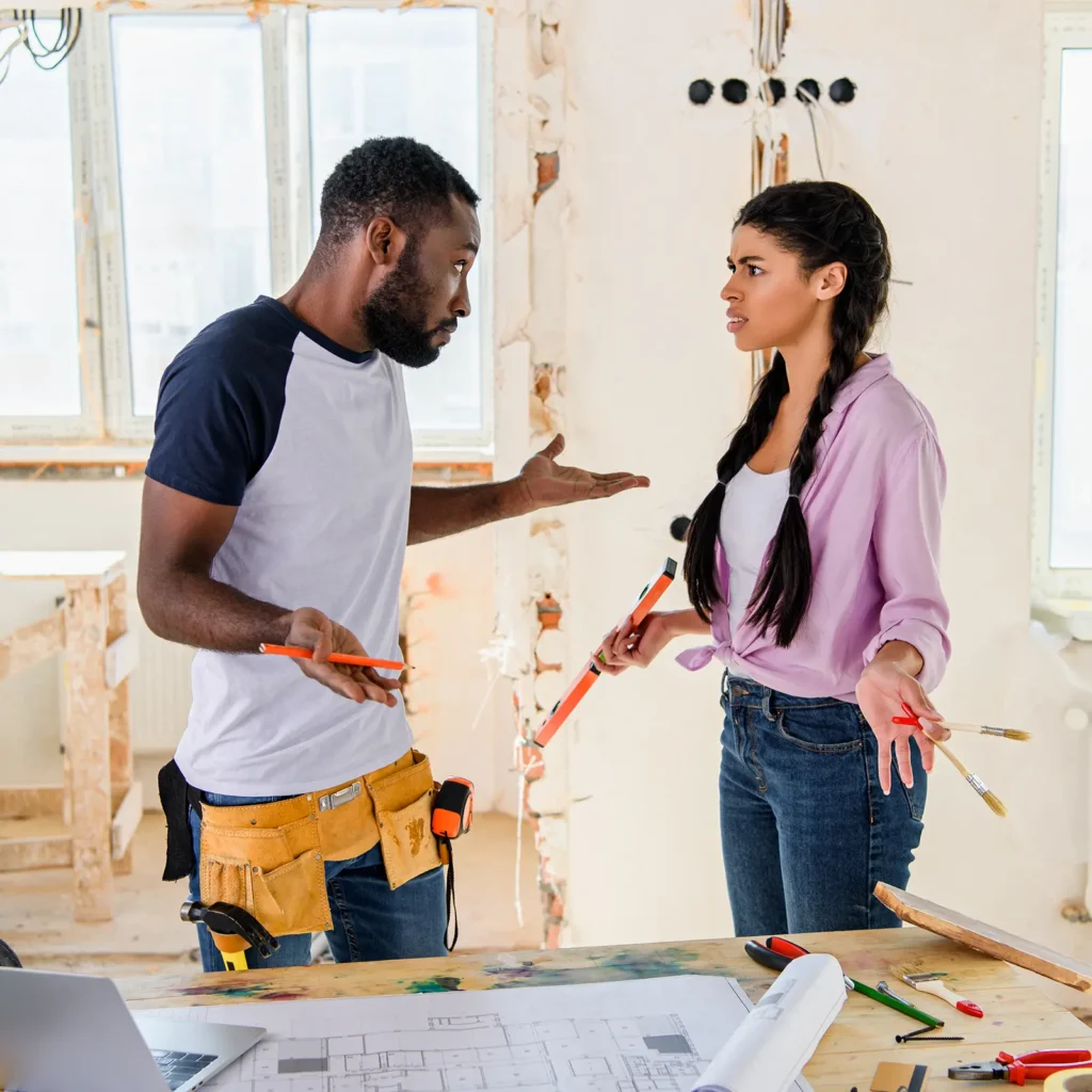 DIY vs. Professional Demolition: What You Need to Know. Featuring a photo of a young couple arguing in the middle of their do-it-yourself demolition project, with drywall stripped and wires dangling from holes.