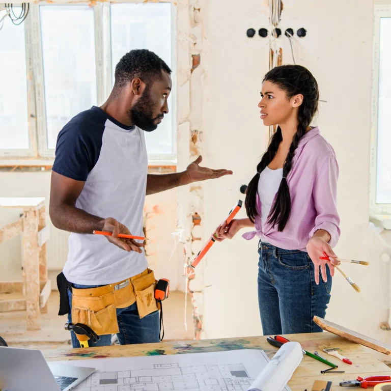 DIY vs. Professional Demolition: What You Need to Know. Featuring a photo of a young couple arguing in the middle of their do-it-yourself demolition project, with drywall stripped and wires dangling from holes.