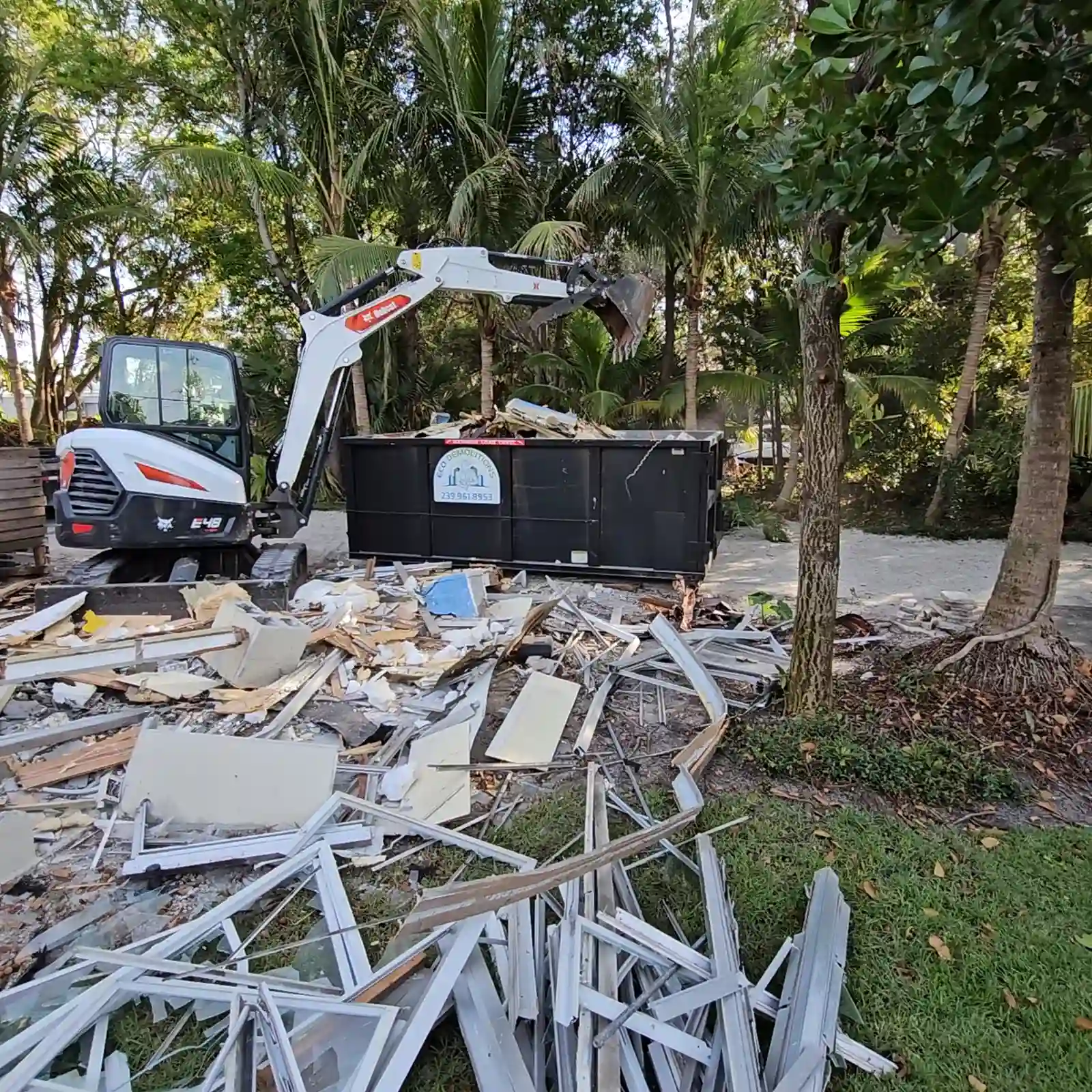 The Benefits of Compact Dumpster Rentals for Tight Spaces. Featuring a photo of an Eco Demolitions Bobcat backhoe dumping demolition debris into a compact dumpster on a residential job site in Southwest Florida.