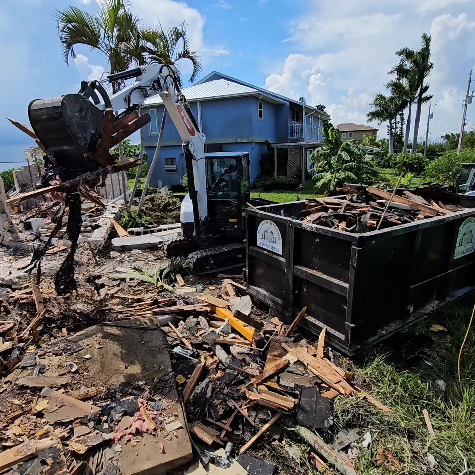 Choosing the Right Dumpster Size for Your Naples Project. Featuring a photo of an Eco Demolitions dumpster on a complete demolition site in Southwest Florida, getting filled by a Bobcat backhoe.
