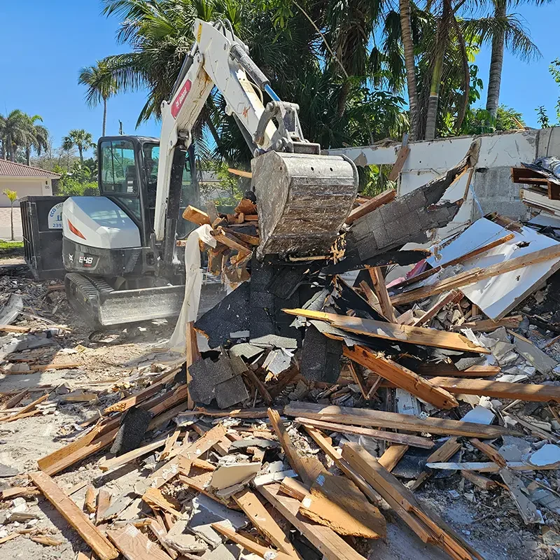 Eco Demolitions Bobcat backhoe working on a residential job site in Southwest Florida, clearing out debris to put in the compact dumpster behind it.