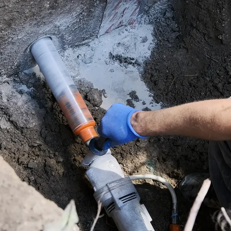 Photo of a construction worker using a very large water-cooled coring drill to drill a hole through a concrete foundation.
