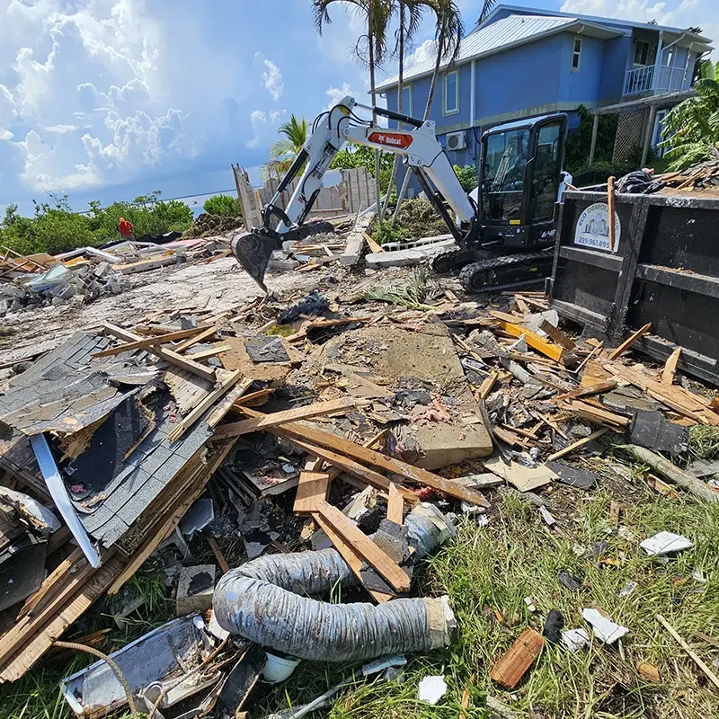 An Eco Demolition backhoe working on a job site, removing deconstruction debris from a Southwest Florida beach residence that has been leveled.