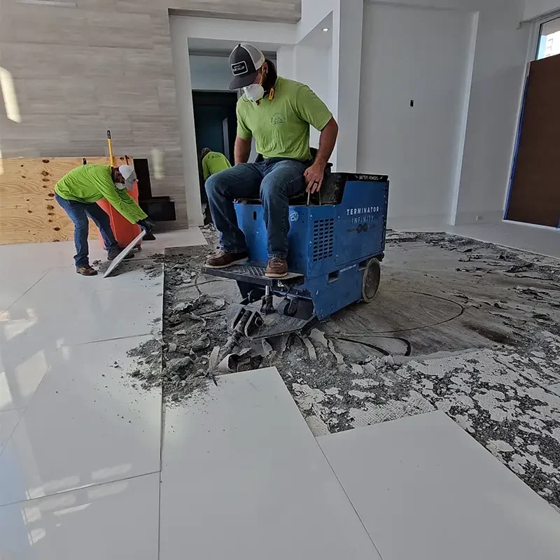 Eco Demolitions employee riding a flooring removal machine to break up the tile floor of a condo in Southwest Florida. Another employee nearby picks up tiles to remove them with his hands.